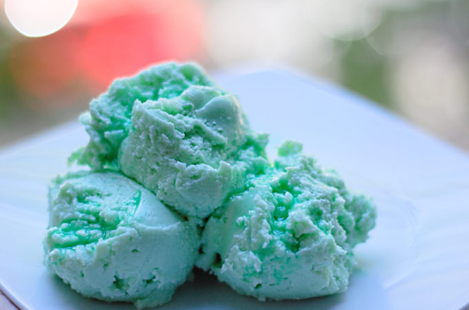 Auf einem Dessertteller sind drei Kugeln grünes Waldmeistereis angerichtet.