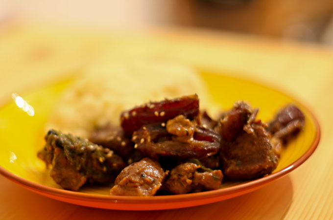 Abbildung eines Tellers, auf dem geschmortes Lammfleisch mit Datteln und Walnüssen sowie Couscous liegt.