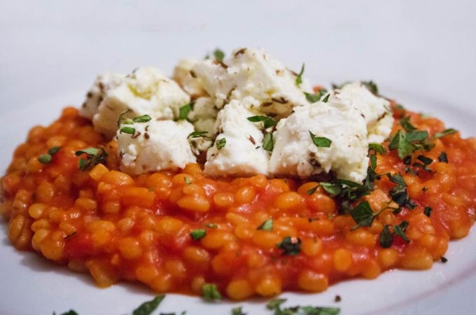 Graupenrisotto in Tomate mit mariniertem Feta, bestreut mit Oregano.