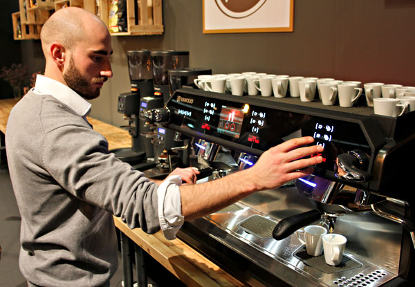 Ein Barista steht vor einer Espressomaschine, wie man sie in Bars findet, und brüht frischen Espresso.