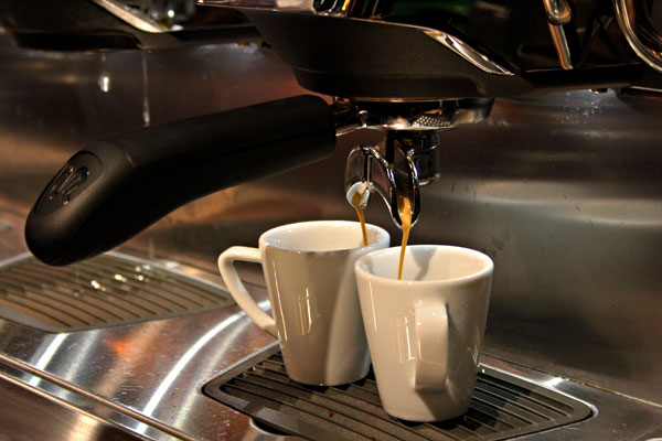 Das Bild zeigt zwei Espressotassen unter einem Siebträger, aus dem frischer Espresso fließt.