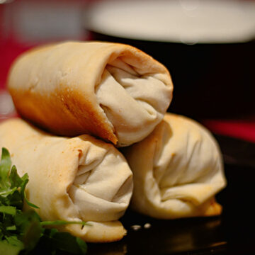 Drei Arabische Pasteten aus knusprigen Filoteig auf einem Teller. Im Hintergrund ein Joghurt-Knoblauch-Dip.