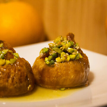 Zwei Feigen im Orangen-Honig-Sud auf einem Teller. Sie sind mit Pistazien gefüllt.