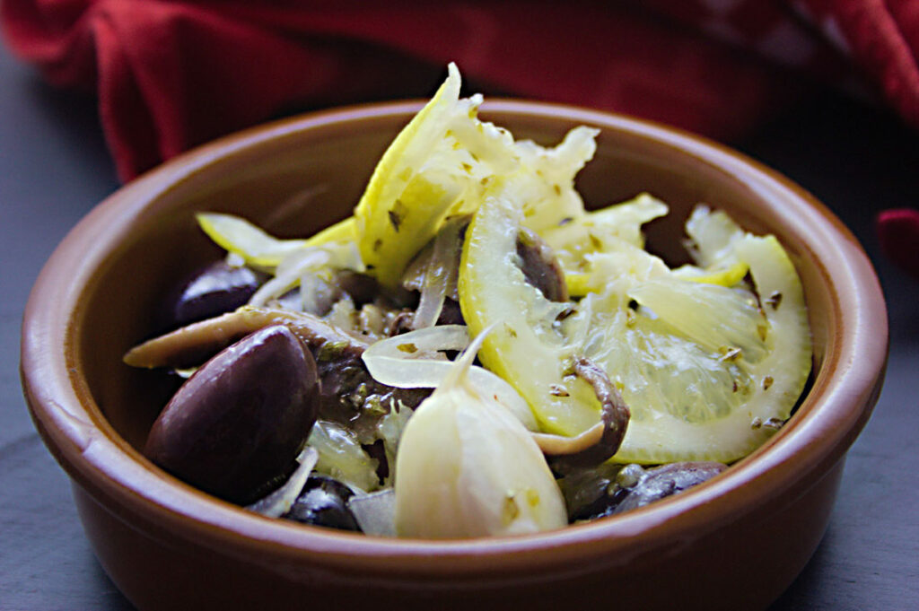 Eine braune Tonschüssel mit marinierten Oliven, Sardellen, Zitronenscheiben und Knoblauch