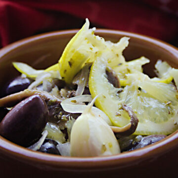 Eine braune Tonschüssel mit marinierten Oliven, Sardellen, Zitronenscheiben und Knoblauch