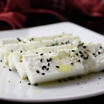 Ein Teller mit Schafskäsescheiben, die mit Scwarzkümmel und Olivenöl mariniert wurden.