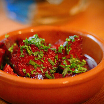 Eine kleine Tonschale mit Chorizo-Stücken in Rotwein. Garniert mit Petersilie.