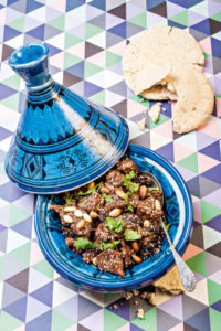 Eine offene blaue Tajine. Sie ist mit Lammfleisch mit Pflaumen und Mandeln gefüllt.