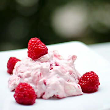 Ein Teller, auf dem das sahnige Semifreddo mit Himbeeren und Baiser angerichtet ist. Dekkoriert mit frischen Himbeeren.