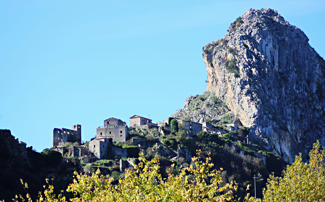 Hoch oben auf dem Berg stehen alte, verlassene Häuser, daneben ein raues Felsmassiv: San Severino di Centola