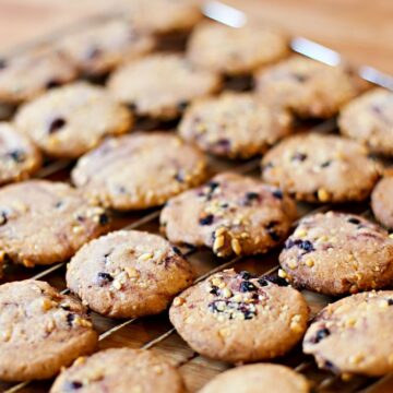 Auf einem Kuchengitter kühlen frisch gebackene Zimtkekse mit Blaubeeren und Cranberries aus.