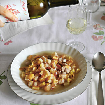 Ein Teller mit Zuppa alla Santé, im Hintergrund wird ein Falanghina in ein Glas eingeschenkt.