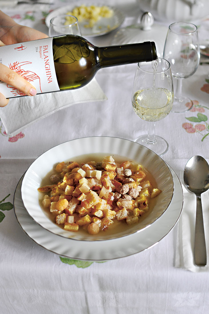 Ein Teller mit Zuppa alla Santé, im Hintergrund wird ein Falanghina in ein Glas eingeschenkt.