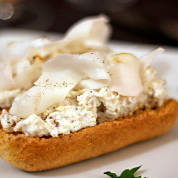 Ein Crostino bestrichen mit Walnussricotta und einer Scheibe Lardo