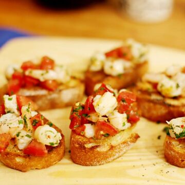 Sechs Bruschettascheiben belegt mit Garnelen und Tomaten