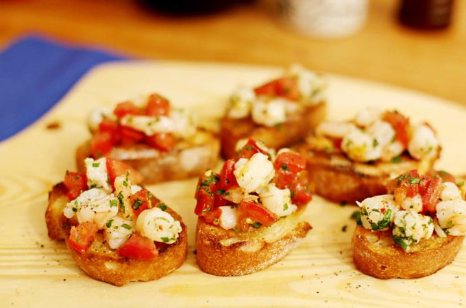 Sechs Bruschettascheiben belegt mit Garnelen und Tomaten