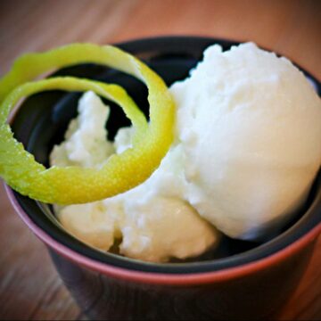 Ein Schälchen mit zwei Kugeln Zitronen-Joghurt-Eis, garniert mit Zitronenschale