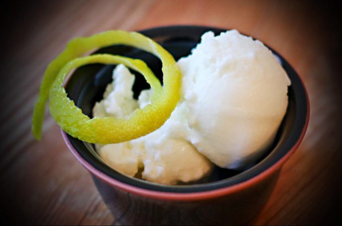 Ein Schälchen mit zwei Kugeln Zitronen-Joghurt-Eis, garniert mit Zitronenschale