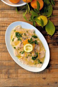 Ein ovaler Teller mit Schwertfisch-Carpaccio, das in einer Mandarinensauce mariniert wurde.