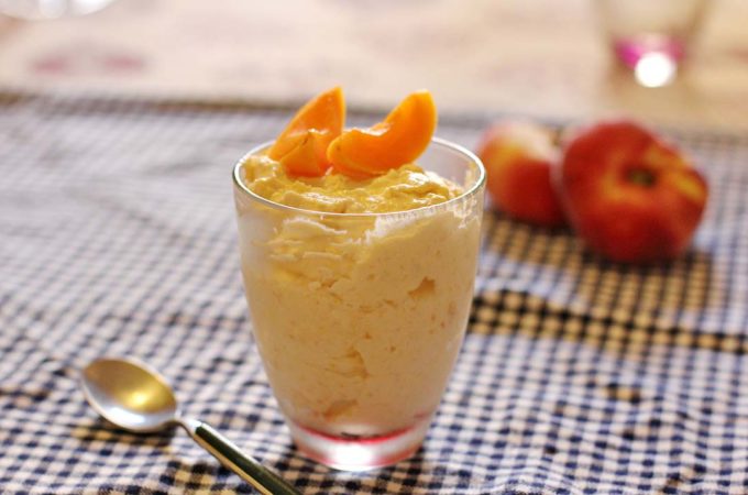 Ein Glas mit Aprikosencreme. Im Hintergrund liegen Pfirsiche.