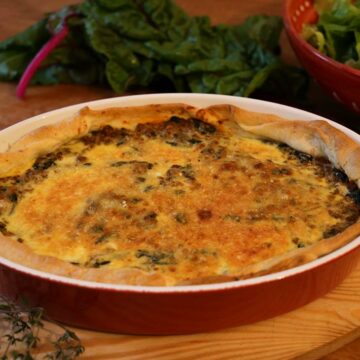 Eine Quiche mit Mangold und Hackfleisch in einer Ofenform auf einem Tablett.