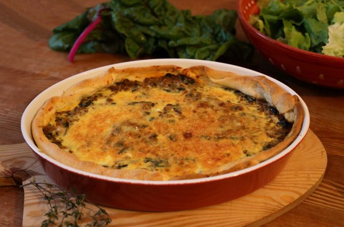 Eine Quiche mit Mangold und Hackfleisch in einer Ofenform auf einem Tablett.