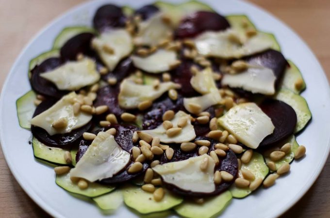 Ein Teller mit einem Carpaccio aus Rote Bete, Zucchini und Scamorza, bestreut mit Pinienkernen.