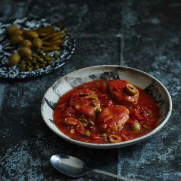 Ein Teller mit Gefilte Fisch in einer mexikanischen Tomaten-Oliven-Kapern-Sauce.