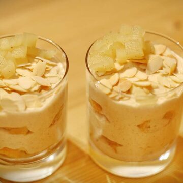 Zwei Dessertgläser mit Apfel-Zimt-Tiramisu, garniert mit Mandelblättchen und Apfelwürfeln.