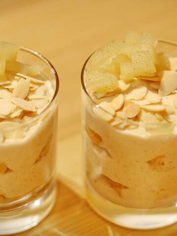 Zwei Dessertgläser mit Apfel-Zimt-Tiramisu, garniert mit Mandelblättchen und Apfelwürfeln.