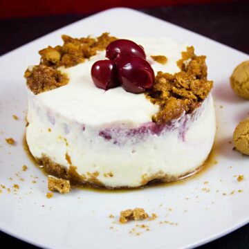 Ein Teller mit einem runden Stück Kirsch-Marzipan-Tiramisu, garniert mit Amarettini