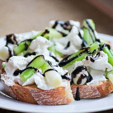 Ein Teller mit vier Scheiben Bruschetta mit Ziegenkäse, Frühlingszwiebeln und Balsamicocreme