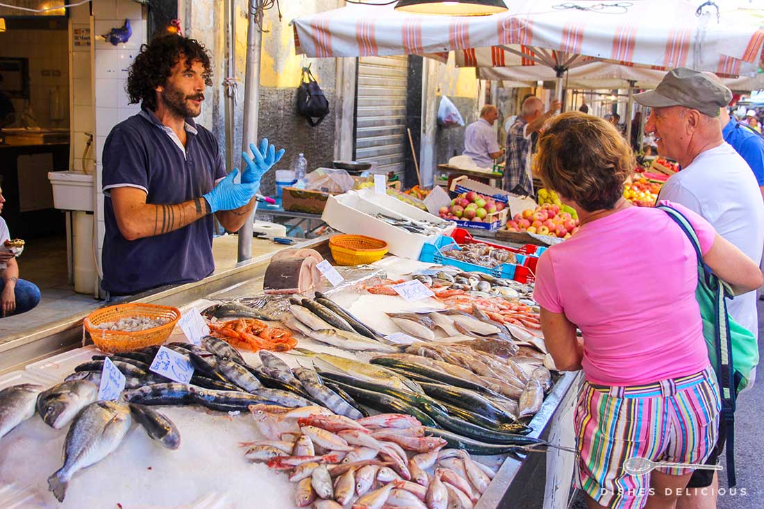 Ein Fischstand auf dem Markt von Syrakus. Der Fischverkäufer unterhält sich mit seinen Kunden.