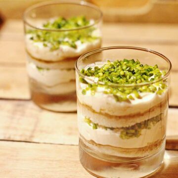 Zwei Gläser mit dem arabischen Cremedessert Aish El Saraya auf einem Holbrett.