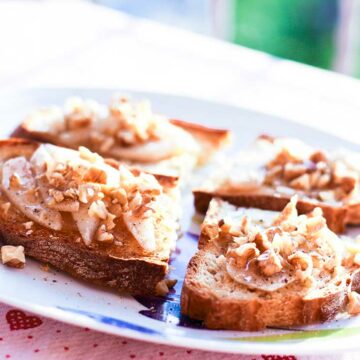Auf einem Teller liegen vier Bruschetta-Scheiben belegt mit Birne, Walnuss und Pecorino