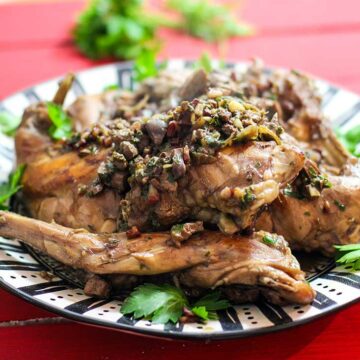 Auf einem Teller ist geschmortes Kaninchenfleisch angerichtet und mit Petersilie garniert.