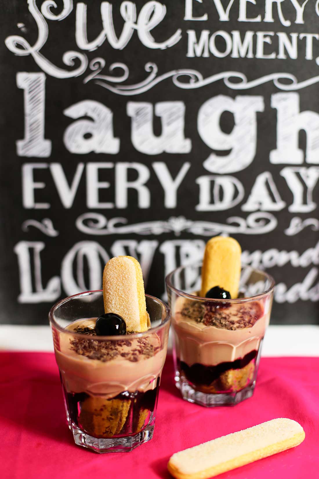 Zwei Dessertgläser mit Schoko-Tiramisu, garniert mit Amarenakirschen und Löffelbiskuits.