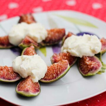 Ein Teller mit frisch aufgeschnittenen Feigen, auf denen kleine Nocken Mascarponecreme liegen.