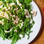 Ein Salat mit Rucola, Garnelen und Mozzarella, daneben liegen zwei Tomaten