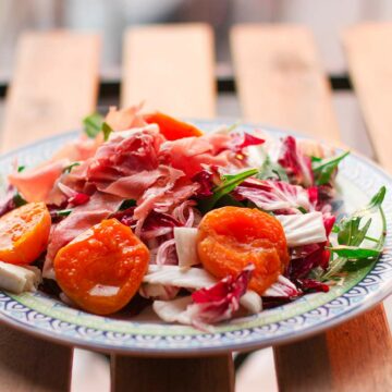 Ein Teller mit Salat, garniert mit Aprikosen und Schinken