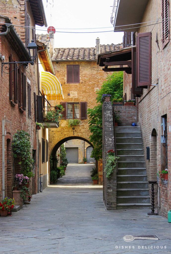 Foto einer Gasse in Buonconvento. Eine Treppe führt zu einem Hauseingang, im Hintergrund verbindet ein Bogen zwei Häuser.