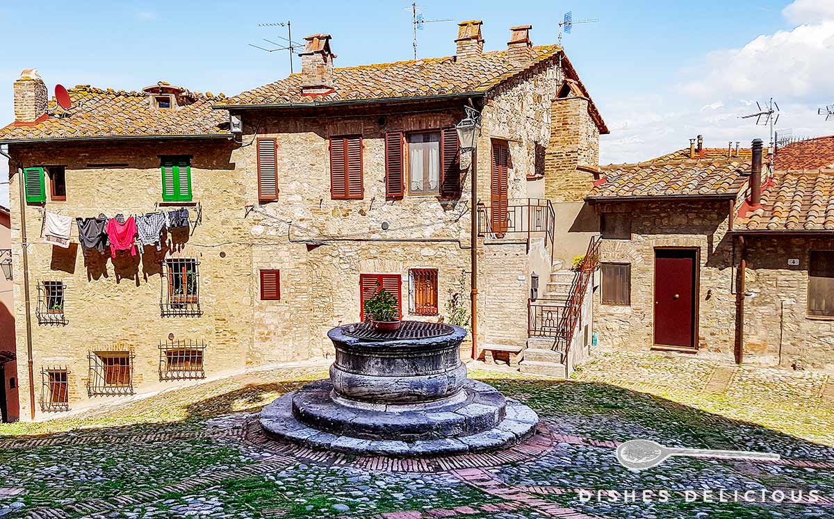 Foto eines mittelalterlich wirkenden Platzes in Castiglione - im Zentrum steht ein alter Brunnen.