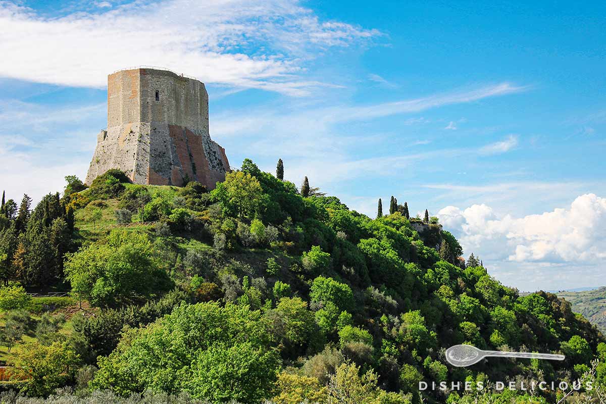 Foto vom Festungsturm Rocca di Tentennano auf einem bewaldeten Hügel.
