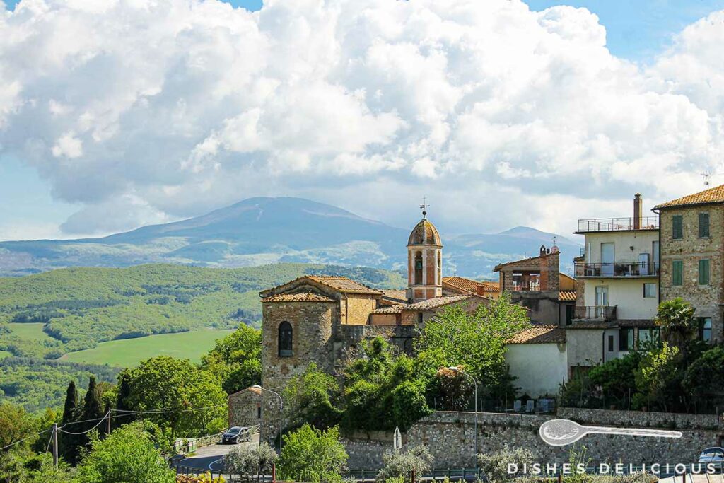 Foto von der Kirche Santi Stefano e Degna in Castiglione d'Orcia, im Hintergrund die Landschaft der Toskana.