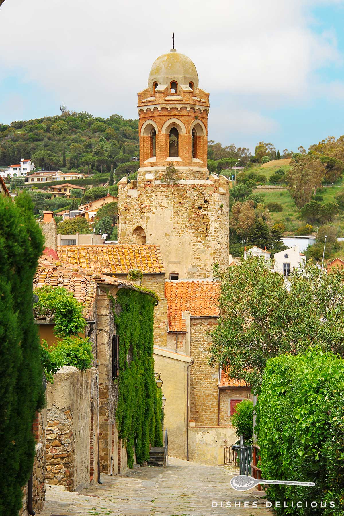 Foto der Kirche Giovanni Battista in Castiglione della Pescaia, zu der ein gepflasterter Weg führt.