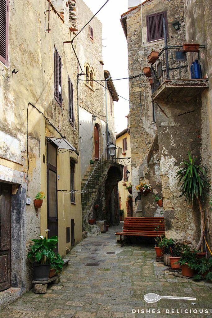 Foto einer engen Gasse in Capalbio, vor einem Haus steht eine Sitzbank.