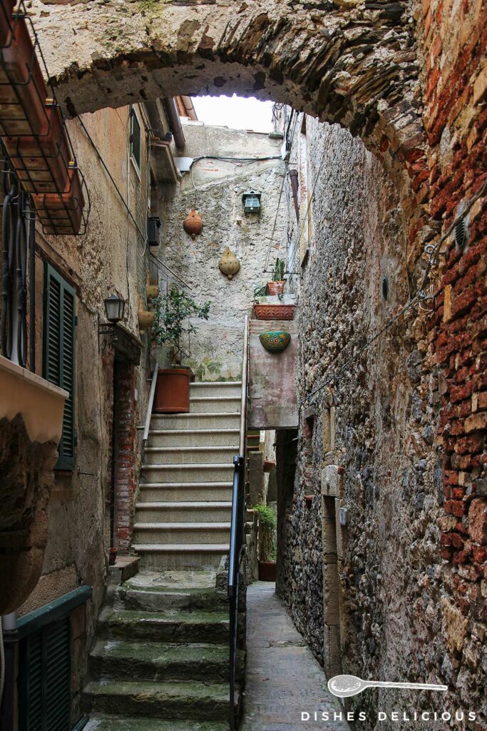 Foto einer sehr engen Gasse, die durch eine Treppe zu einem Hauseingang zusätzlich verschmalert wird.