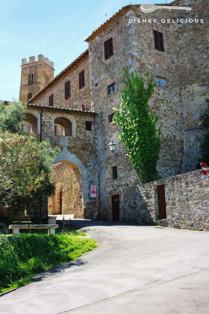 Foto des alten Stadttors San Giorgio in Montemerano, im Hintergrund ragt ein Turm in die Höhe.