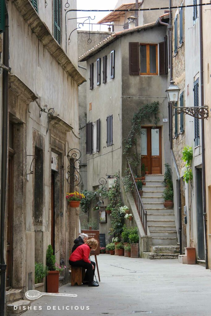 Foto einer Gasse in Pitigliano, zwei Frauen sitzen vor einem Haus uns unterhalten sich.