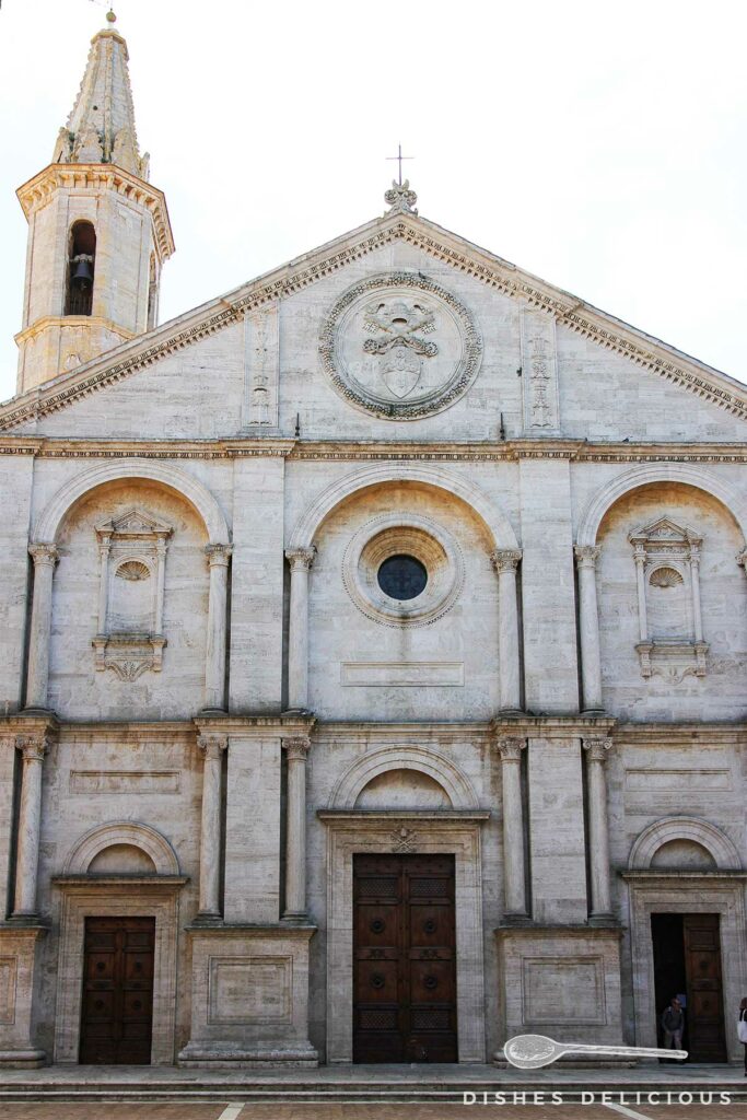 Foto von der Frontfassade des Doms von Pienza. Drei große Bögen prägen die Fassade.